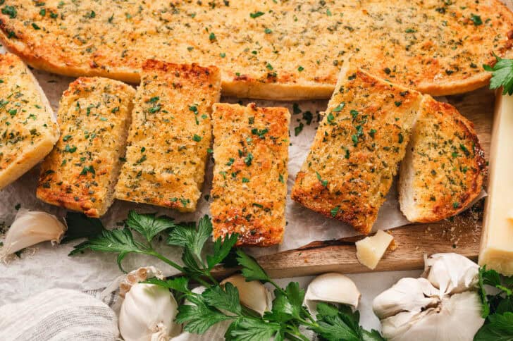 A loaf of garlic bread in oven on a wooden cutting board on a light surface.