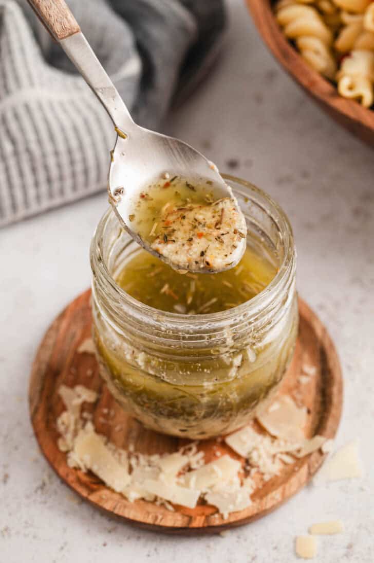 A spoon lifting homemade Italian dressing out of a glass jar.