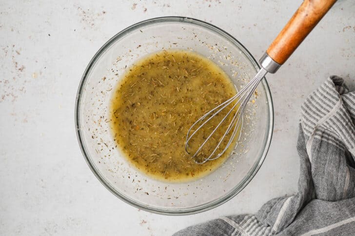 A glass bowl filled with an herby oil mixture with a whisk in it.