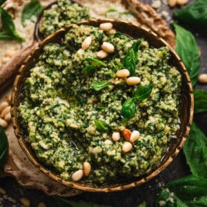 A bowl of homemade pesto sauce garnished with pine nuts and fresh basil.