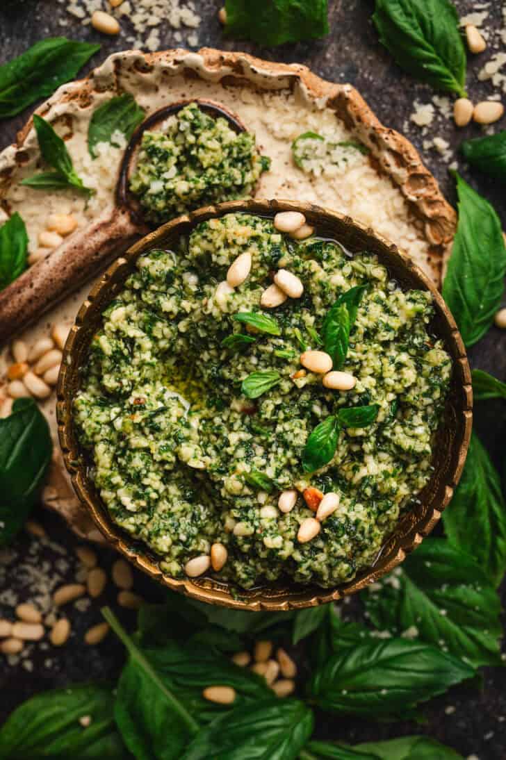 A bowl of homemade basil pesto garnished with pine nuts and fresh basil.