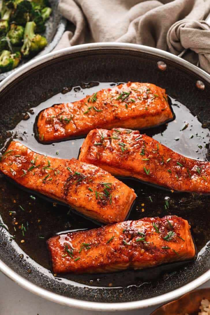 Four pieces of salmon with honey glaze in a skillet.