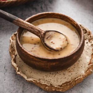 A wooden bowl filled with honey mustard dressing, with a wooden spoon lifting some out.