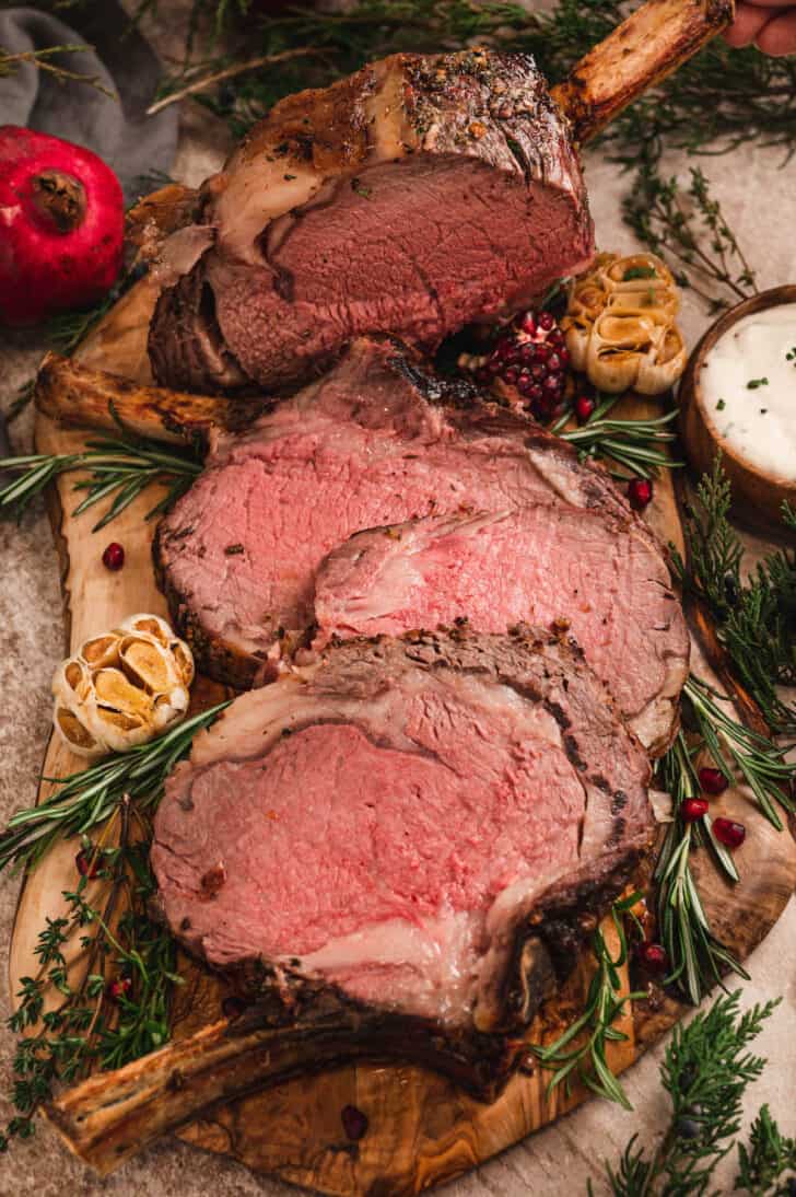 A prime rib recipe, cut into thick slices on a rustic wooden cutting board.