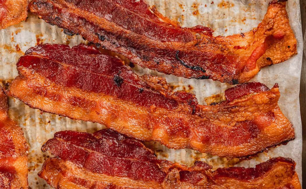 Crispy bacon lined up on a parchment paper lined baking pan.