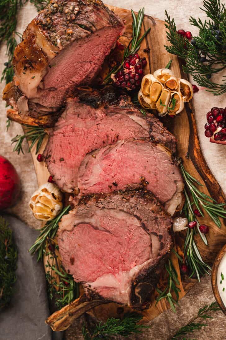 A prime rib recipe, cut into thick slices on a rustic wooden cutting board.