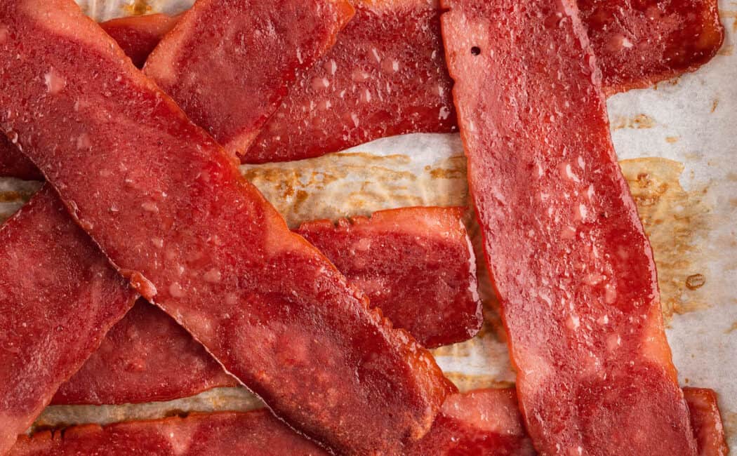 Oven baked turkey bacon slices sitting on top of a rimmed baking pan.