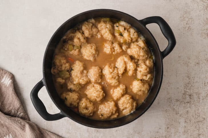 A cast iron dutch oven filled with stew covered in dumplings.