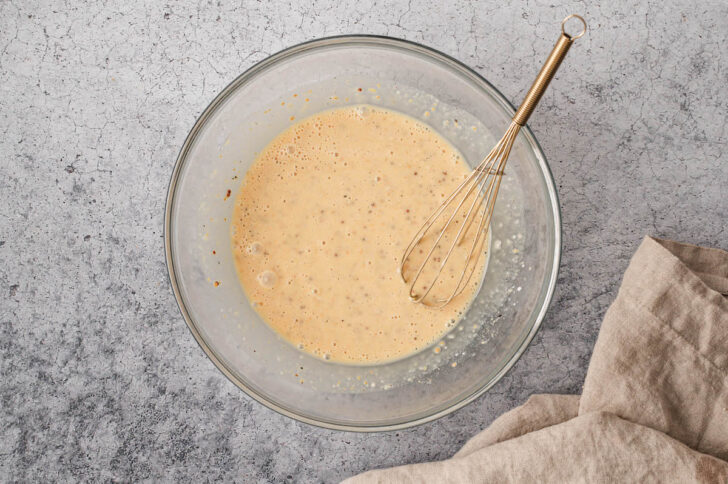 A glass bowl filled with a golden yellow mixture with a whisk in it.