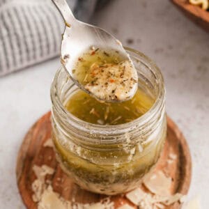 A spoon lifting homemade Italian dressing out of a glass jar.