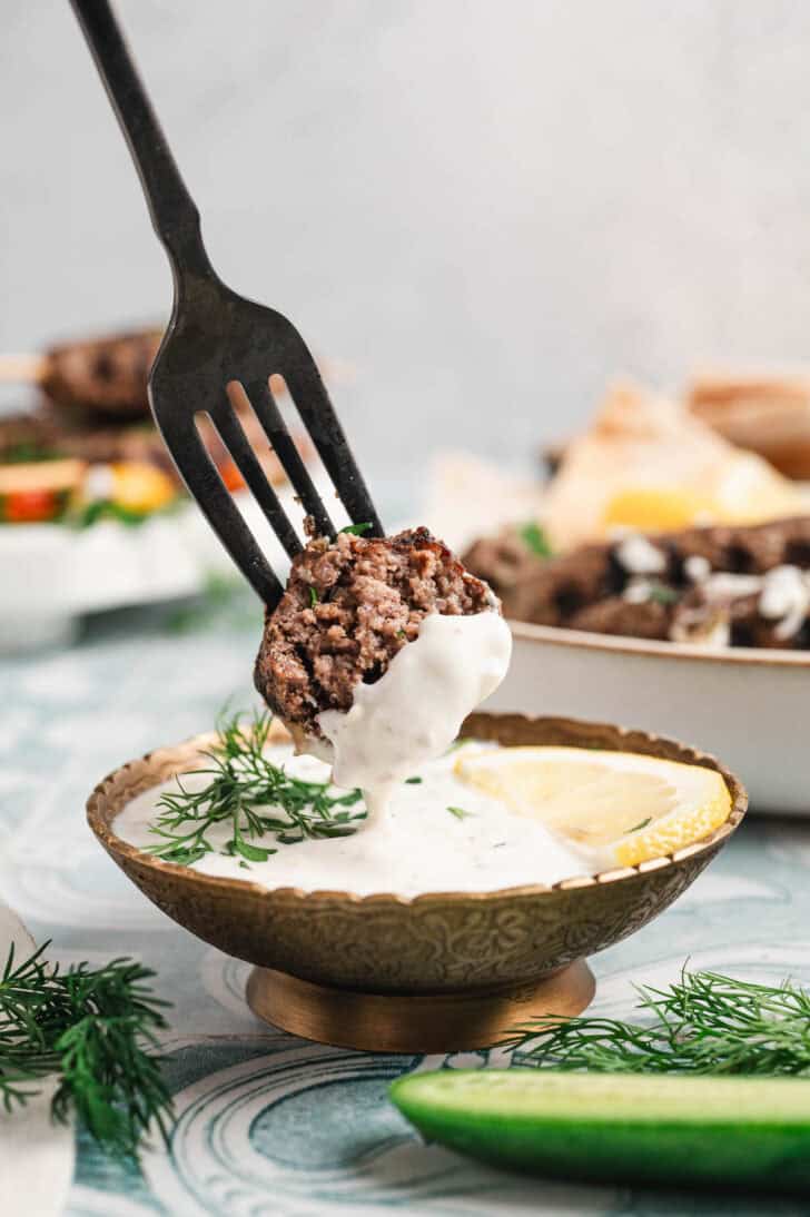 A fork dipping kafta beef into a creamy dipping sauce.