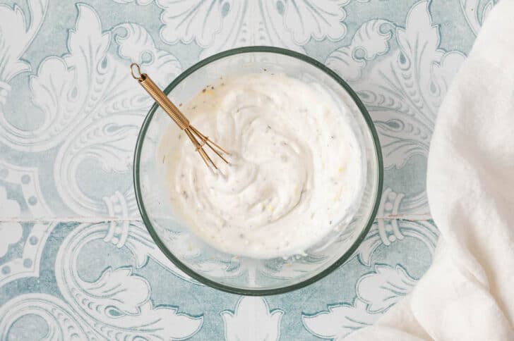 A glass bowl filled with a creamy sauce, with a whisk in it.