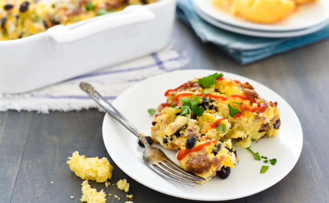 Egg casserole on small white plate. Crumbled cornbread next to plate.