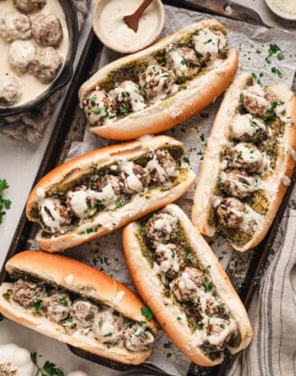 Five meatball sandwiches on a rimmed baking pan.