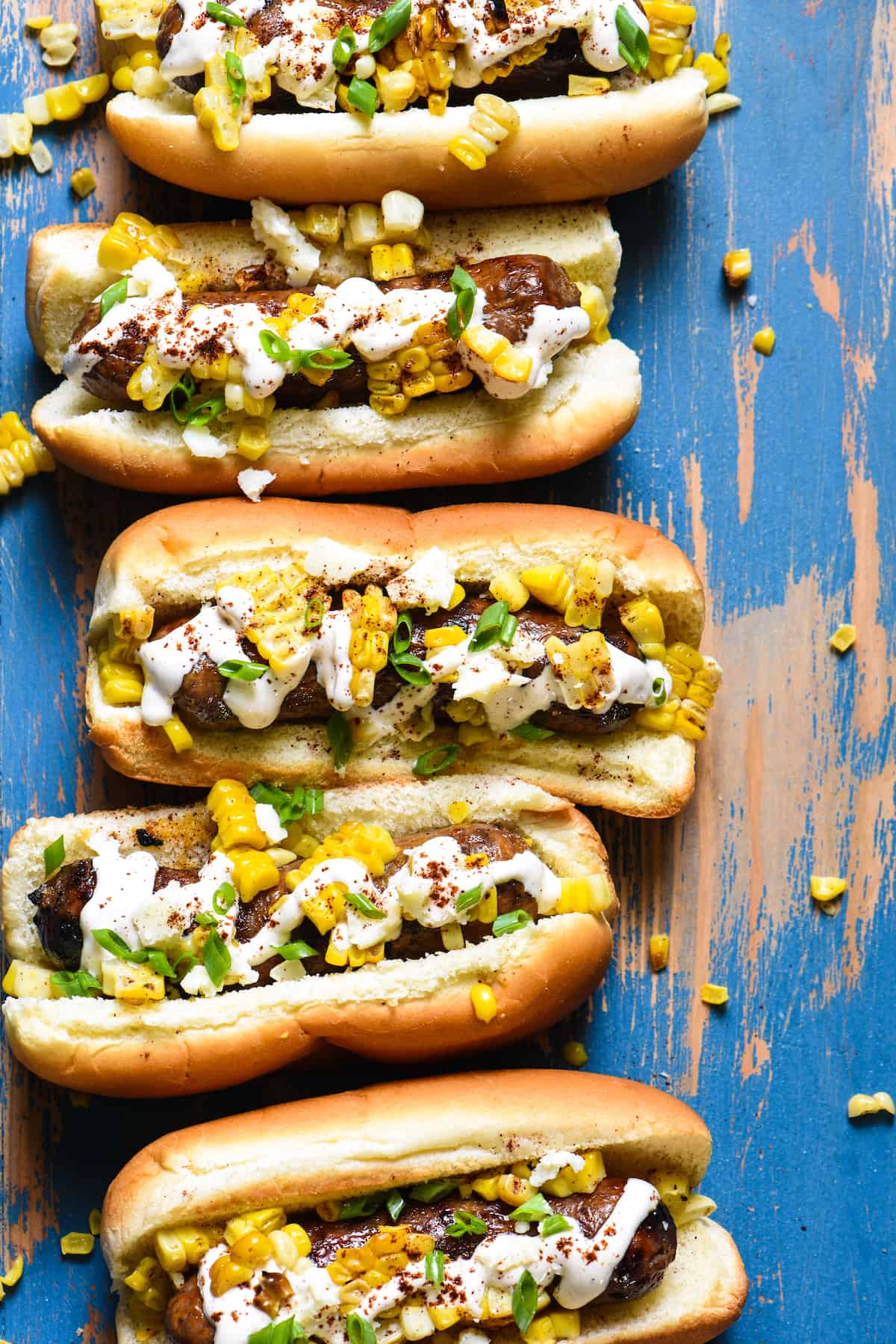 Inspired by elote, these Mexican Street Corn Brats are ideal for a summer celebration or easy weeknight meal! Spicy sausages are topped with fresh sweet corn, creamy lime sauce and tangy cheese. | foxeslovelemons.com