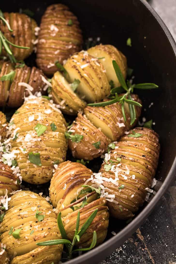 Mini Hasselback potatoes sprinkled with rosemary in a cast iron skillet.