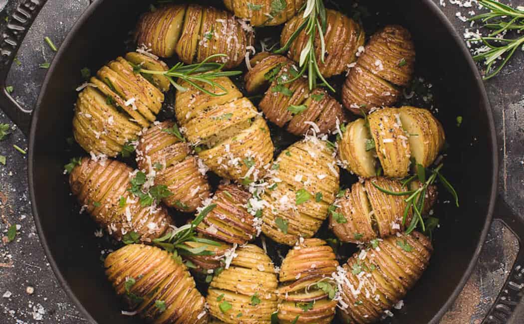 Mini Hasselback potatoes in a cast iron skillet, sprinkled with rosemary sprigs and shredded Parmesan cheese.