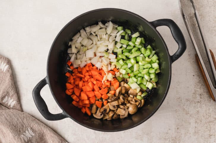 A black cast iron dutch oven filled with mirepoix and mushrooms.