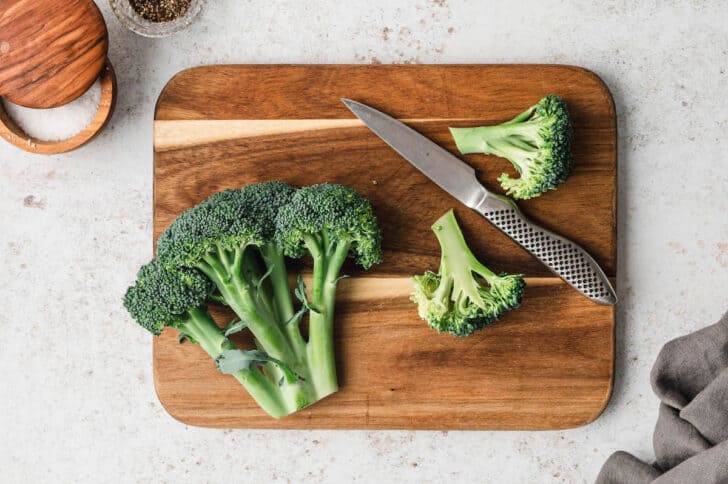 A head of broccoli being cut into florets on a wooden cutting board.