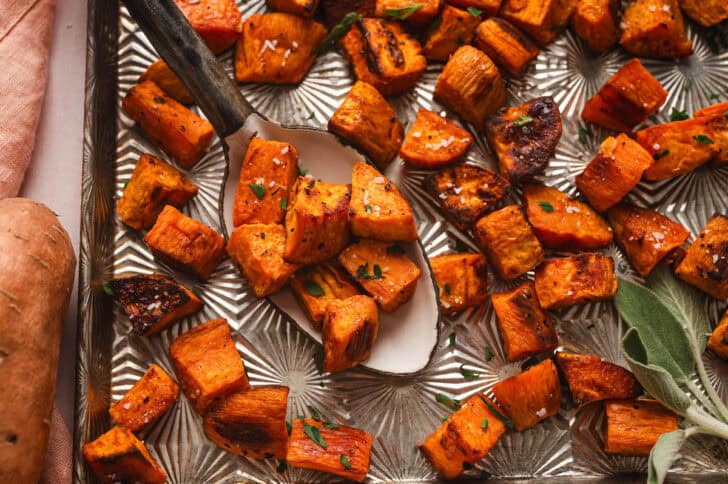 Roasted sweet potato cubes on a serving spoon on a textured baking pan.