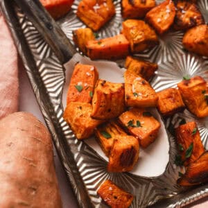 Oven roasted sweet potatoes on a serving spoon on a textured baking pan.