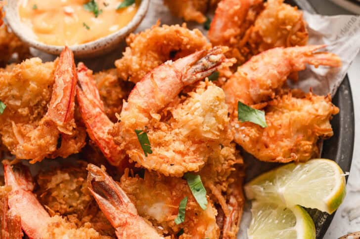 A recipe for coconut shrimp being served with lime wedges and dipping sauce.