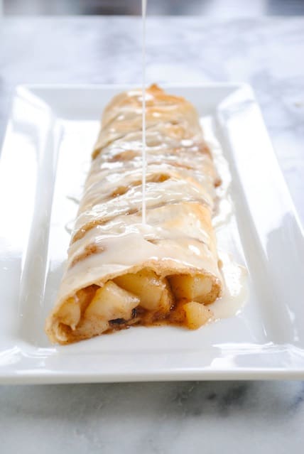 Pear Strudel on rectangular white plate being drizzled with white glaze.