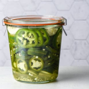 Jar of pickled jalapenos against light background.