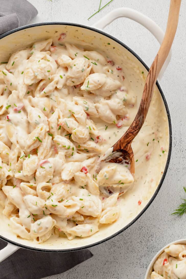 A white Dutch oven filled with pimento mac and cheese, with a wooden spoon stirring it.