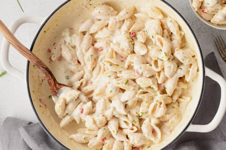 A white Dutch oven filled with pimento mac and cheese, with a wooden spoon stirring it.