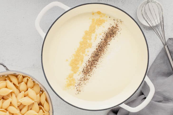 A white Dutch oven filled with a cream sauce topped with ground mustard and black pepper.