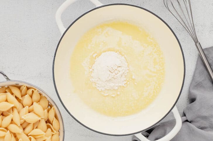 A white Dutch oven filled with melted butter and a scoop of flour.