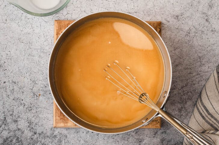 A stainless steel saucepot filled with brown gravy, with a whisk in it.