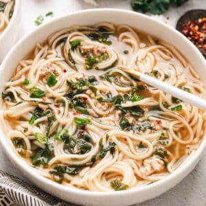 A shallow white bowl filled with pork soup with noodles.