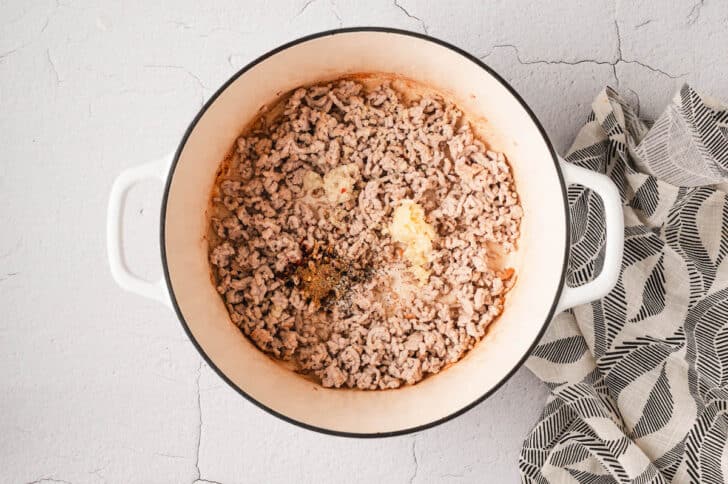 A white Dutch oven filled with cooked ground meat sprinkled with spices.