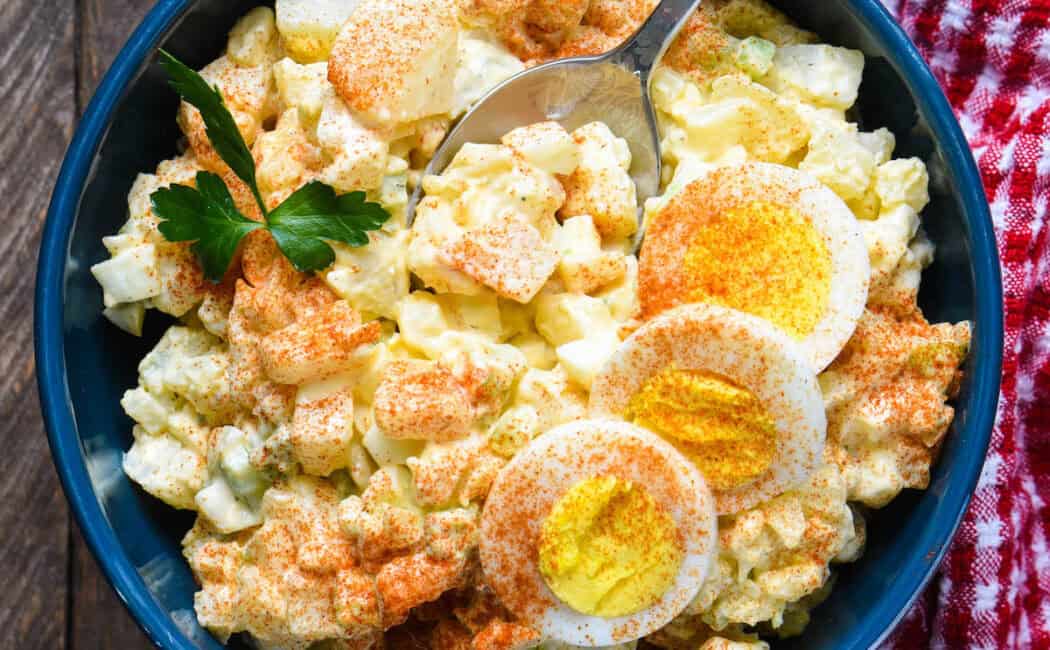 A blue bowl filled with potato salad with egg.