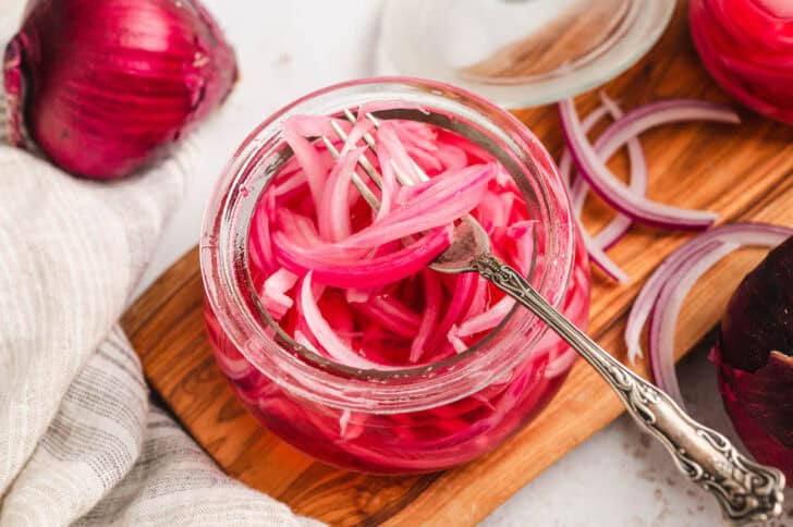 A glass jar filled with easy pickled red onions, with a fork lifting some out.