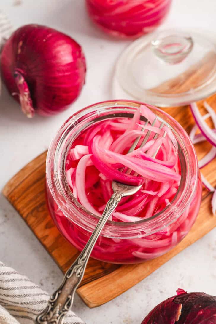 A glass jar filled with quick pickled red onions, with a fork lifting some out.