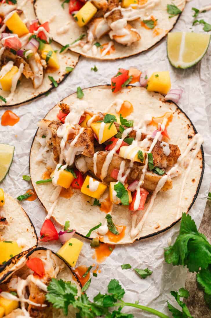 The best fish taco recipe topped with fruit salsa and drizzled with creamy sauce.