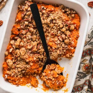 A black spoon lifting a scoop of easy sweet potato casserole out of a white baking dish.