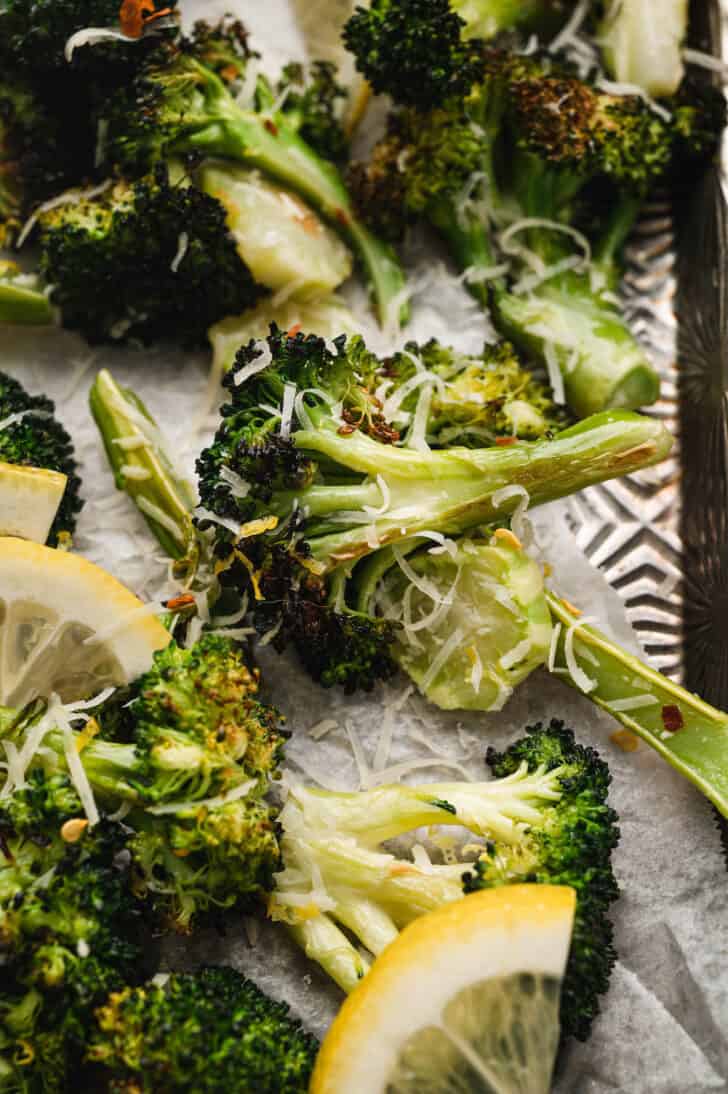 Lemon roasted broccoli with shredded cheese and red pepper flakes on a textured baking pan.