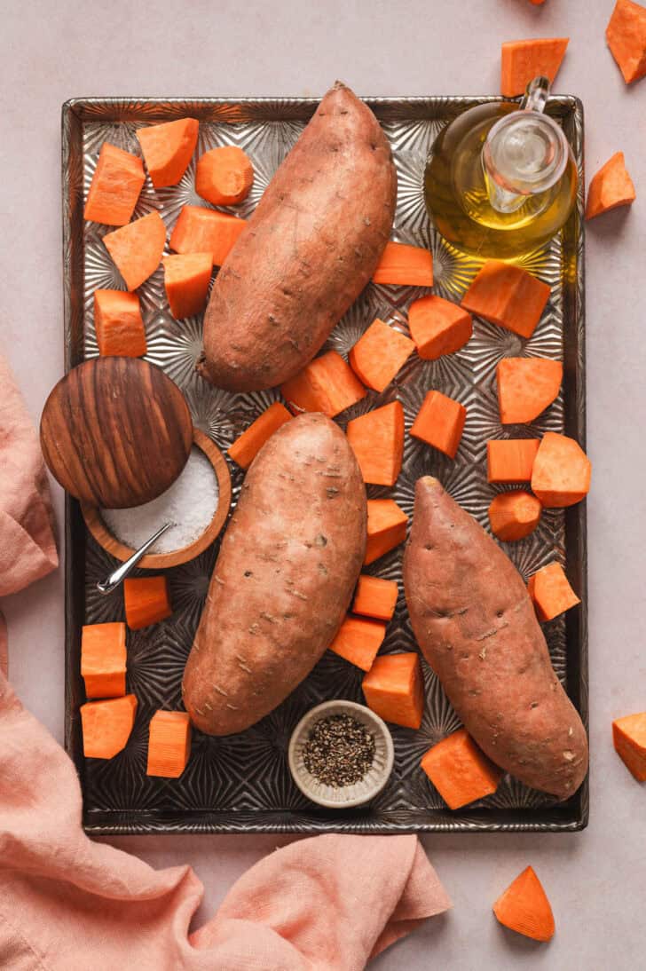 Whole and cubed yams on a baking pan with oil and seasonings.