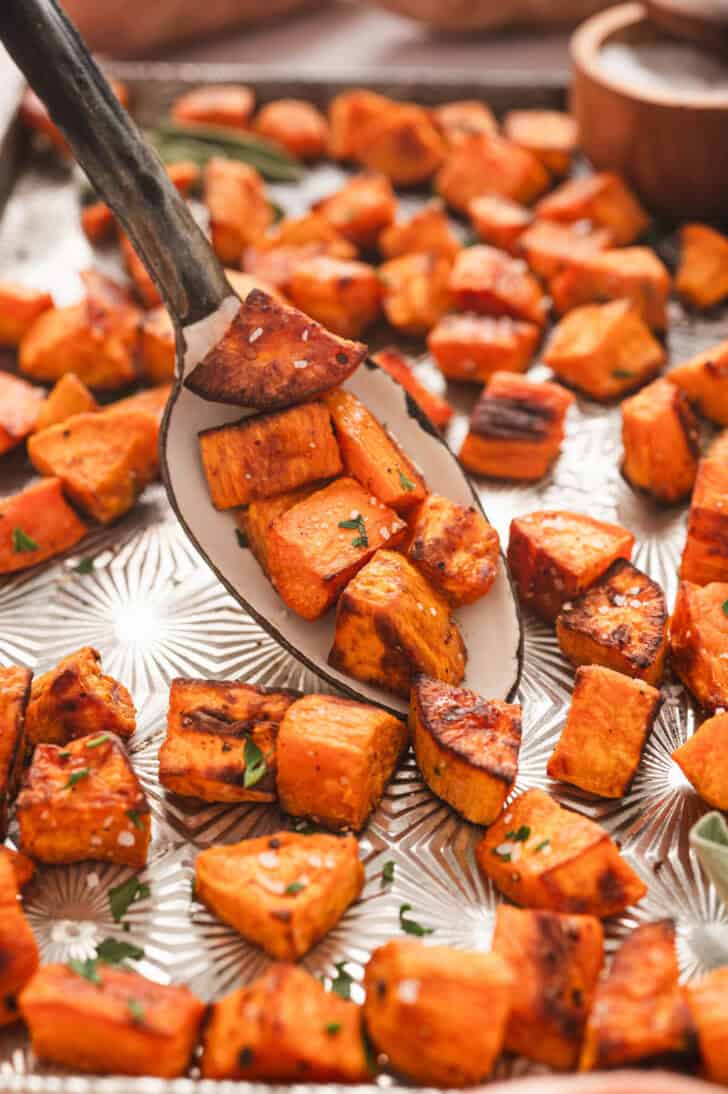 A roasted sweet potatoes recipe on a serving spoon on a textured baking pan.