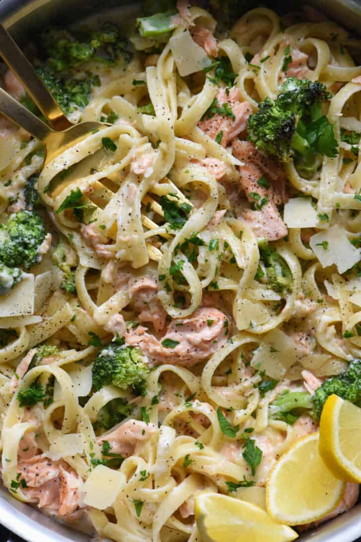 Closeup photo of broccoli and salmon alfredo pasta, with lemon wedge garnishes.