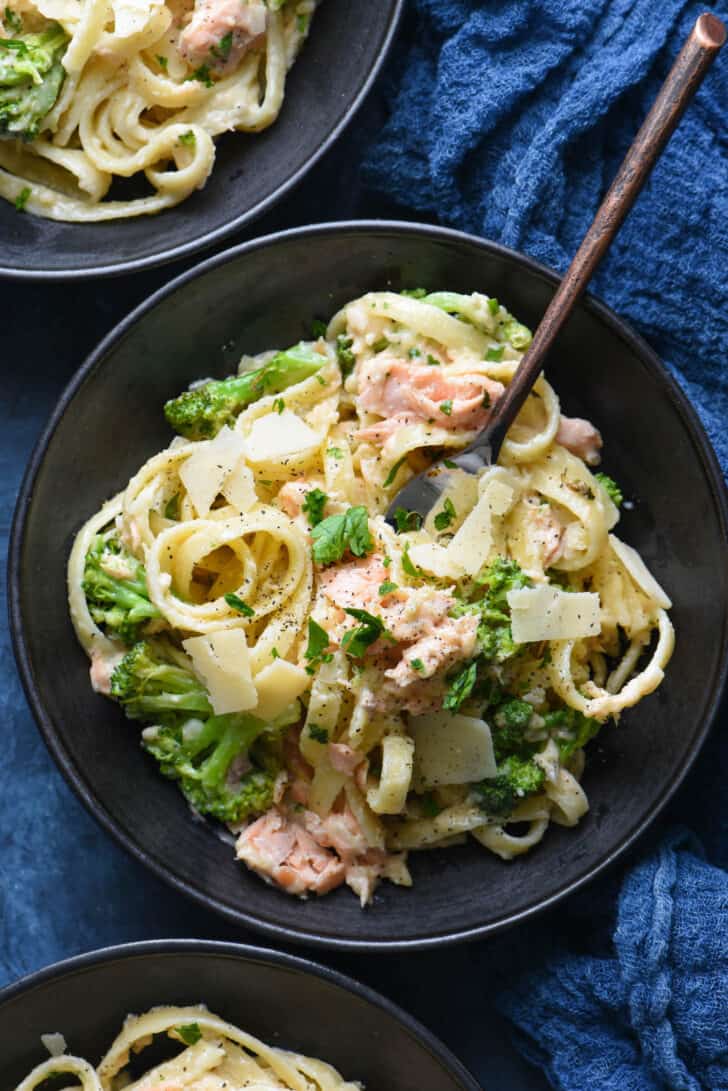 A black bowl filled with salmon alfredo pasta, with a fork digging in.