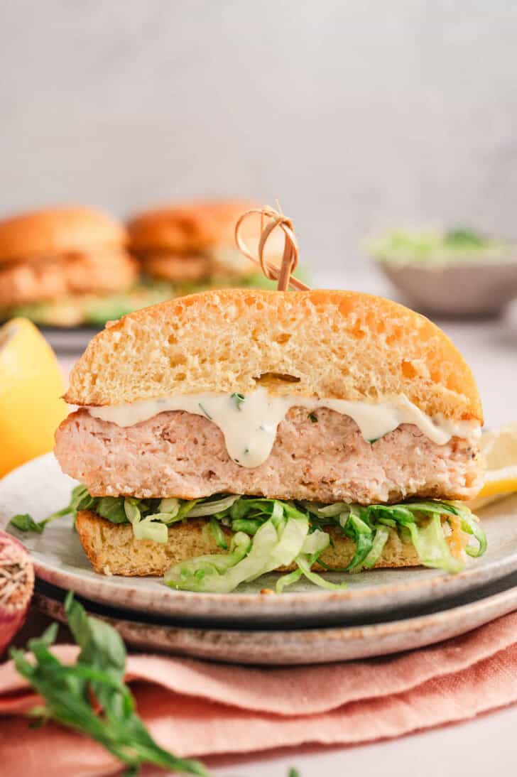 A cross section of a salmon fish burger dressed with tartar sauce and shredded lettuce.