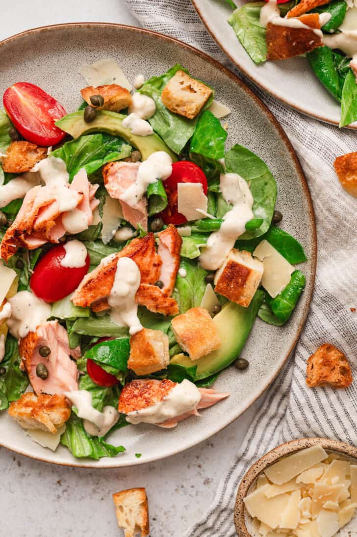 A rustic round plate filled with Caesar salmon salad.