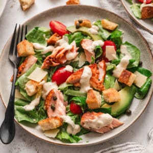 A rustic round plate filled with salmon Caesar salad.