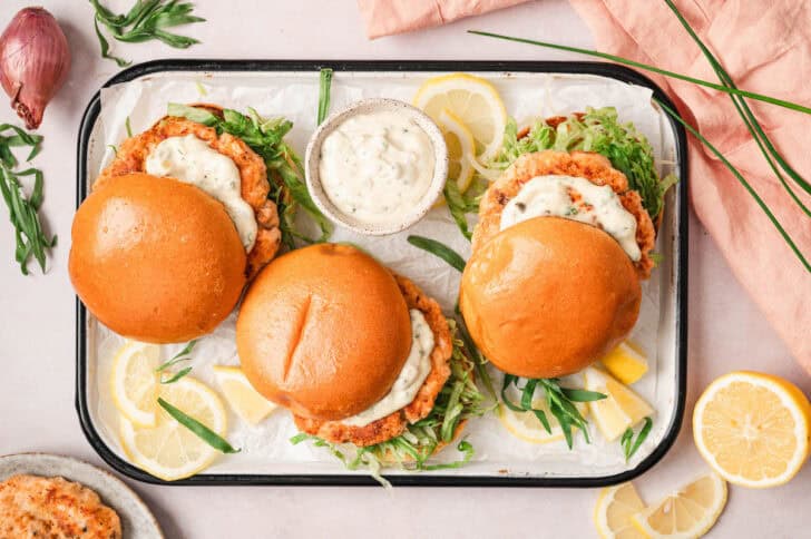 Three salmon burgers on a platter, dressed with tartar sauce and lettuce.