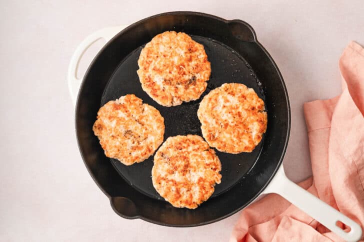 Four fish patties in a cast iron skillet.